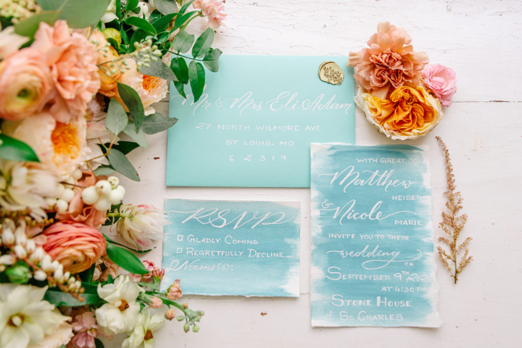 A luxurious hand painted blue watercolor invitation suite lays next to a classic wedding bouquet.