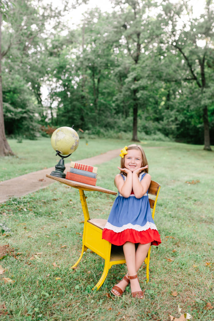You girl sits at yellow desk with globe for back to school photos.