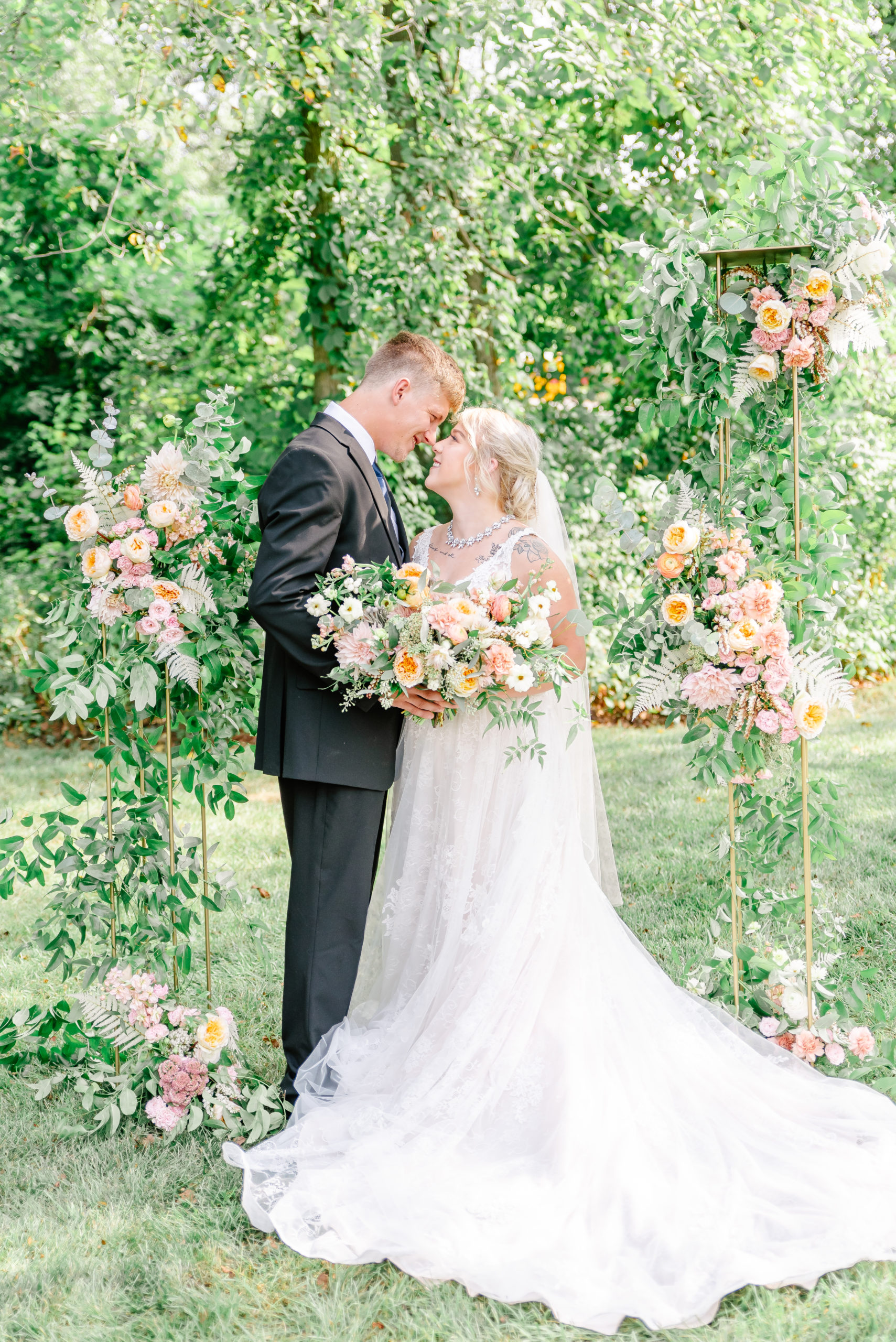 A bride and groom pose with a luxurious floral arbor on their wedding day.