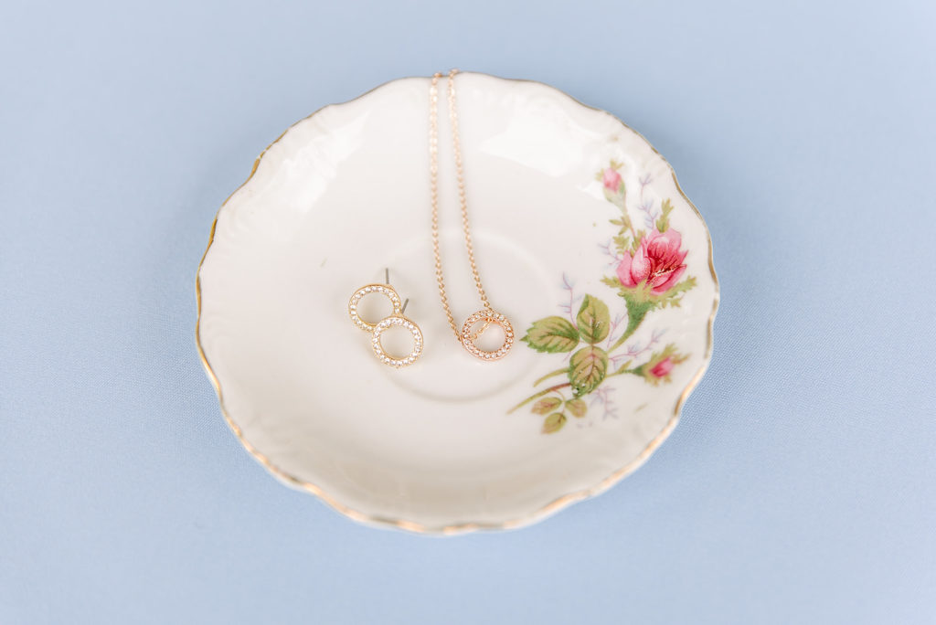 Gold wedding day jewelry lays on a floral trinket dish.