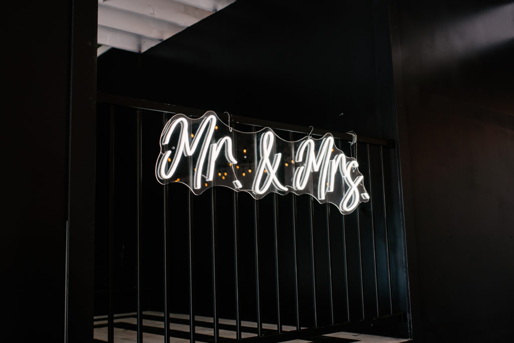 Mr. & Mrs. neon sign hangs on black wall in monochrome wedding venue.