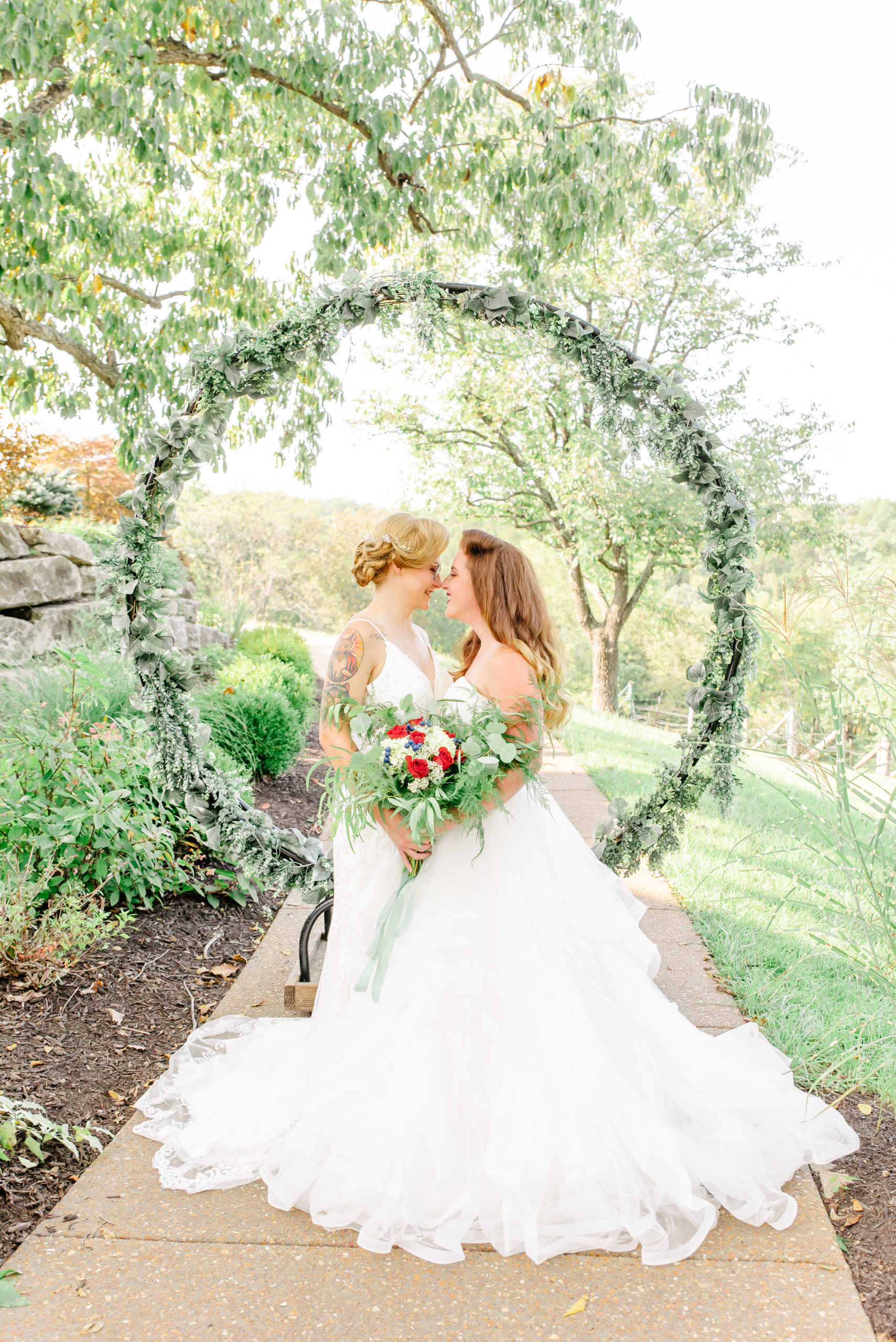 A same sex lesbian couple pose in front of a circle arbor on their wedding day.